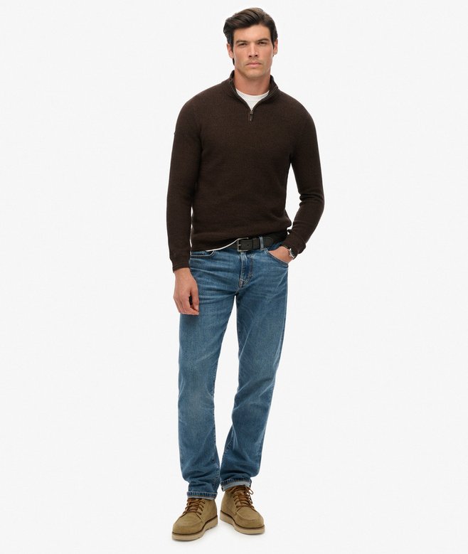 Man wearing a brown sweater, blue jeans, and tan boots on a white background