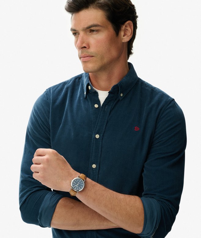 Man wearing a navy blue shirt with a small red logo, standing against a light gray background.
