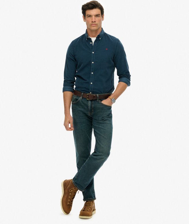 Man wearing a dark blue shirt, jeans, and brown shoes on a white background