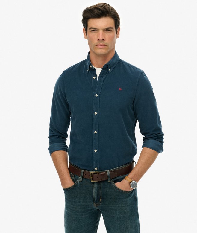 Man wearing a blue button-up shirt with a small red logo on a white background