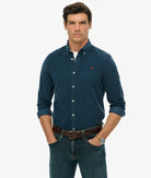 Man wearing a blue button-up shirt with a small red logo on a white background