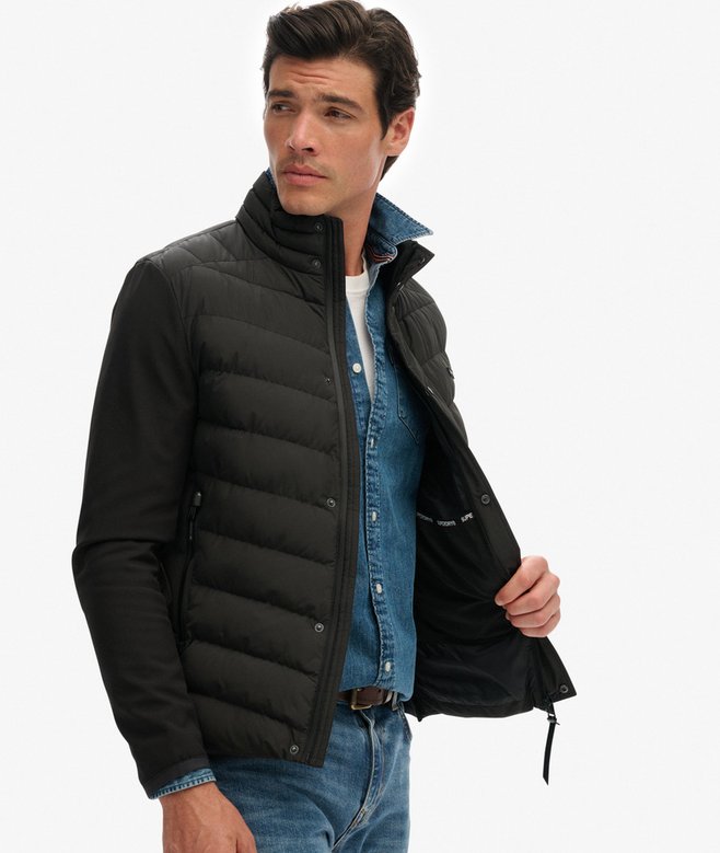 Man wearing a black puffer jacket over a denim jacket on a white background