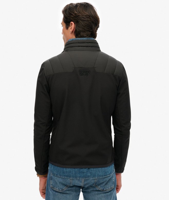 Man wearing a black jacket with a visible brand logo on the back, standing against a white background.