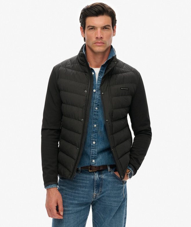 Man wearing a black puffer vest over a blue shirt and jeans on a white background