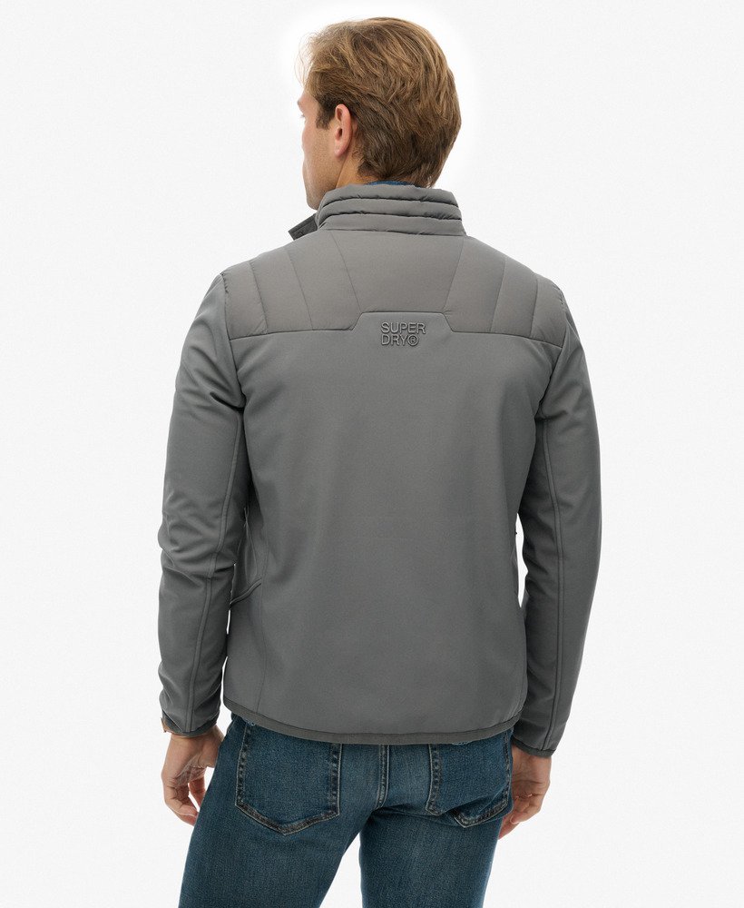 Man wearing a gray jacket with a visible brand logo on the back, standing against a white background.