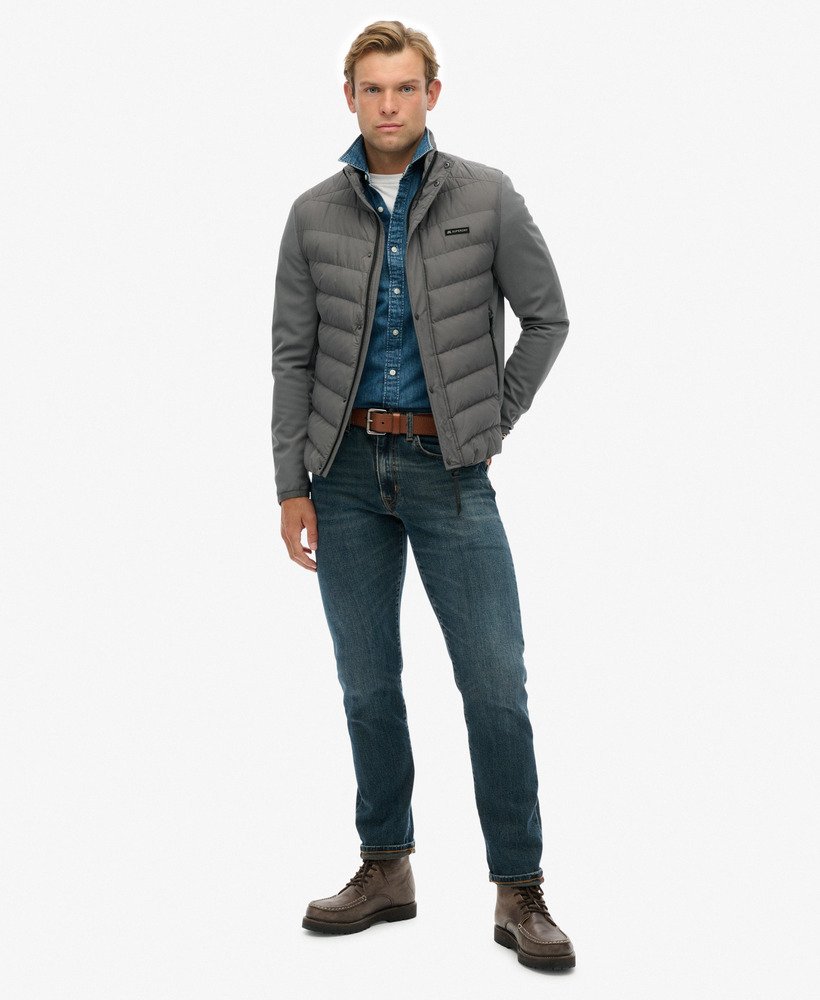 Man wearing a gray puffer jacket, blue denim shirt, and jeans on a white background