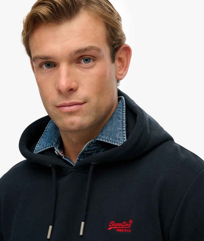 Man wearing a navy hoodie with a visible brand logo on a plain background