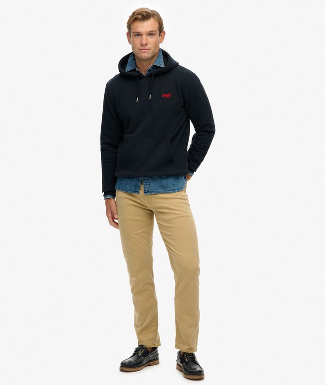 Man wearing a navy hoodie with a logo, blue shirt, and beige pants on a white background