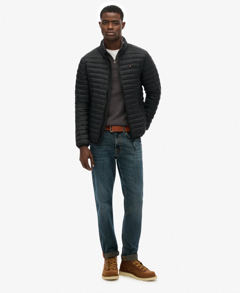 Man wearing a black puffer jacket, dark jeans, and brown boots on a white background