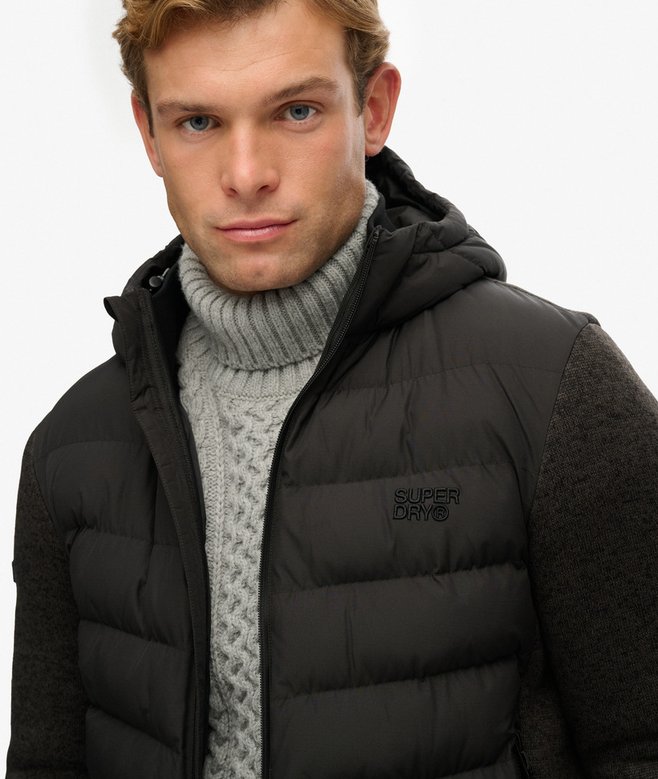 Man wearing a black puffer jacket with a hood and gray turtleneck sweater on a white background