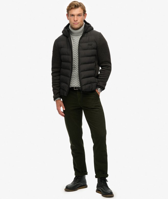 Man wearing a black puffer jacket, gray sweater, and black pants on a white background