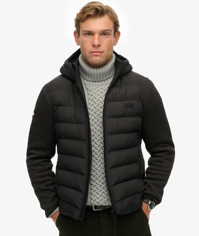 Man wearing a black puffer jacket over a gray sweater on a white background