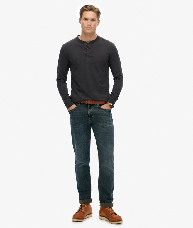 Man wearing a dark gray long-sleeve shirt, blue jeans, and brown shoes on a white background