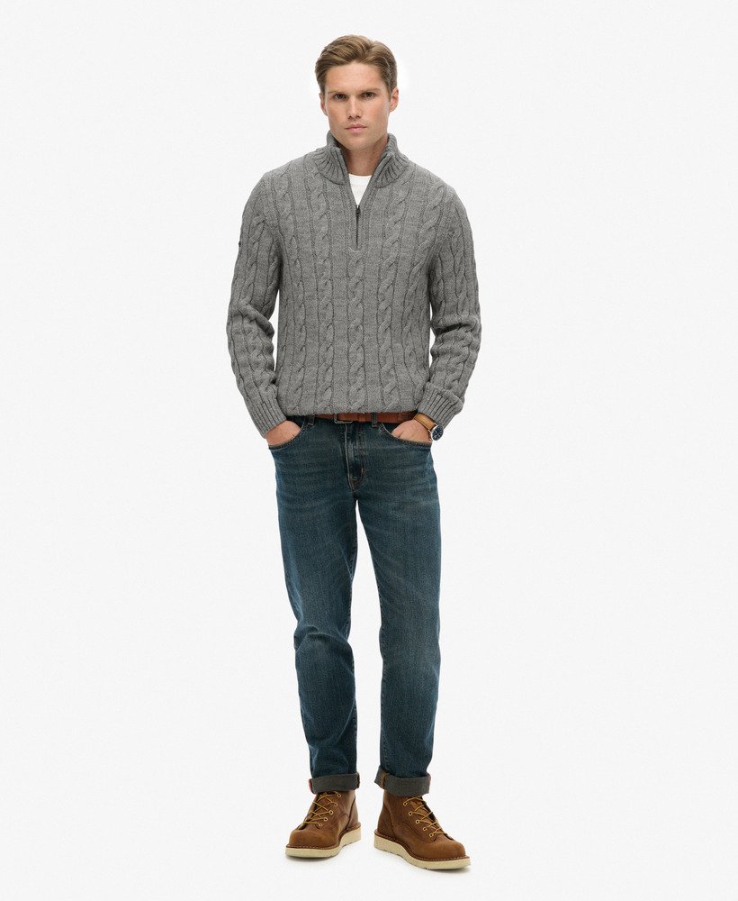 Man wearing a gray cable knit sweater, blue jeans, and brown boots on a white background