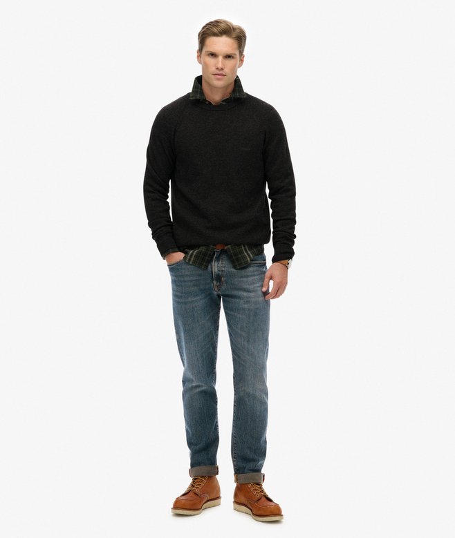 Man wearing a dark grey sweater, blue jeans, and brown boots on a white background