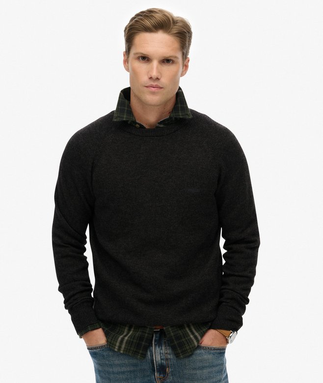 Man wearing a dark grey sweater with plaid collar and jeans on a white background