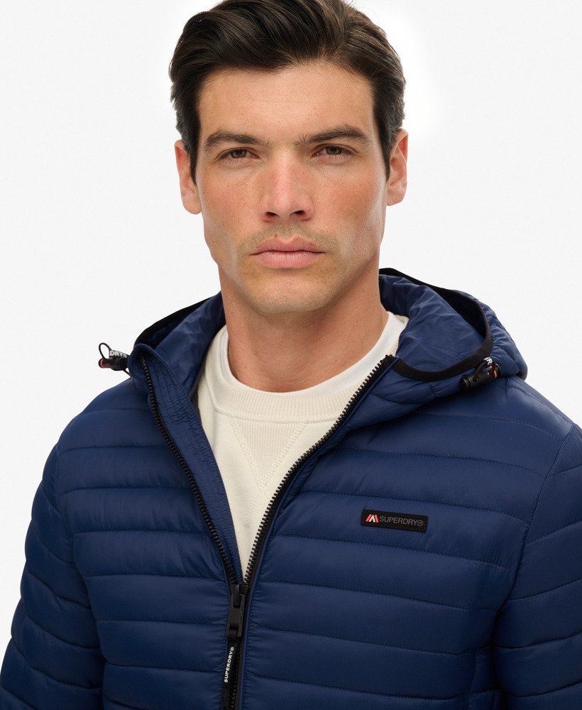 Man wearing a blue puffer jacket with a brand logo on a light gray background