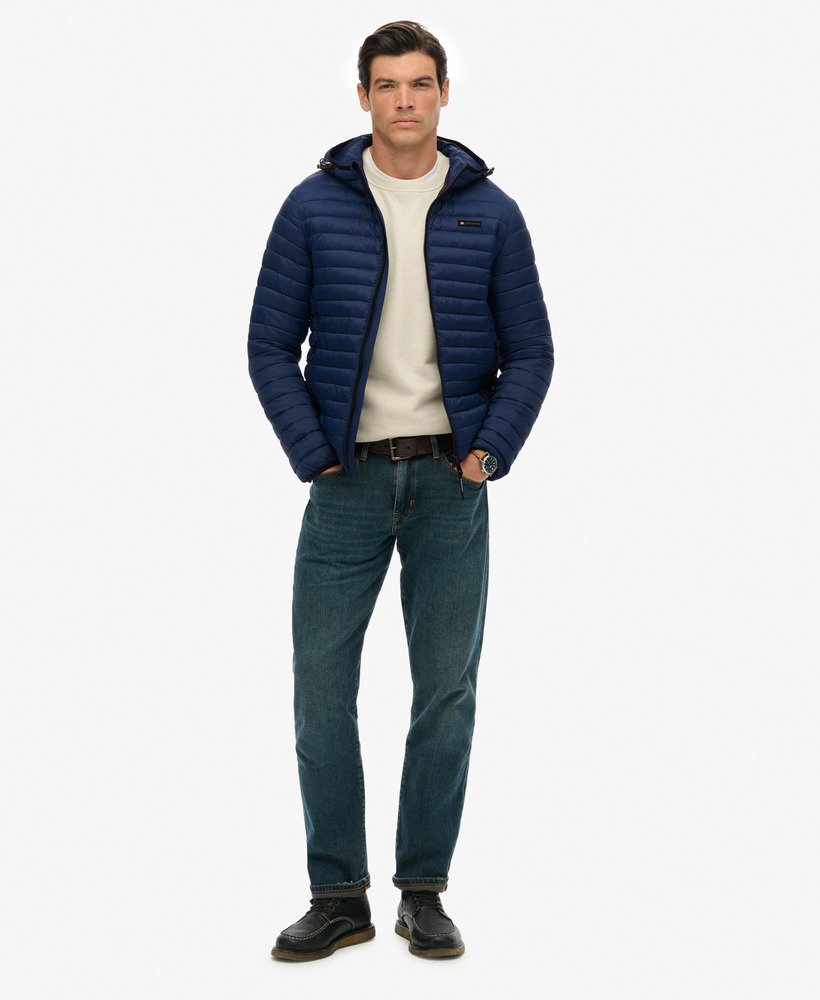 Man wearing a blue puffer jacket, beige sweater, and jeans on a white background