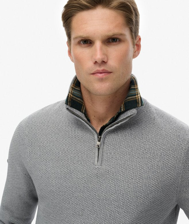 Man wearing a gray quarter-zip sweater with plaid collar on a white background