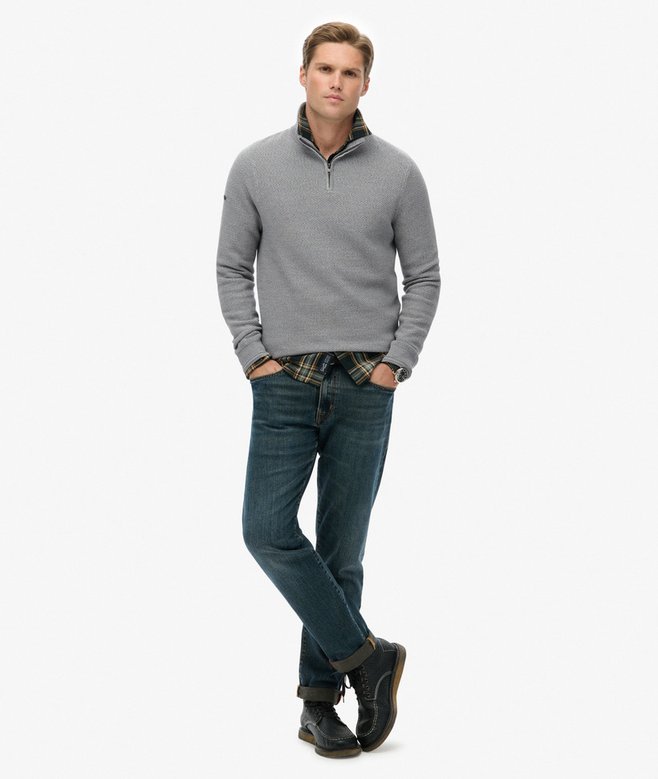 Man wearing a gray sweater and blue jeans on a white background