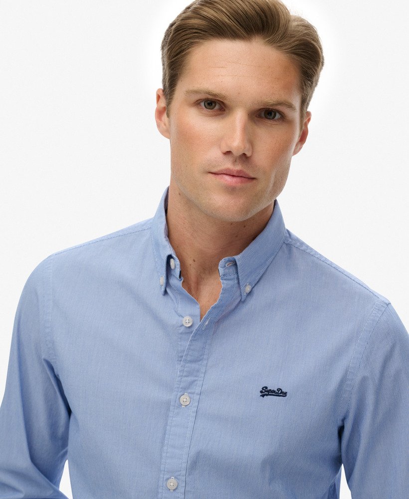 Man wearing a light blue shirt with a brand logo on a white background