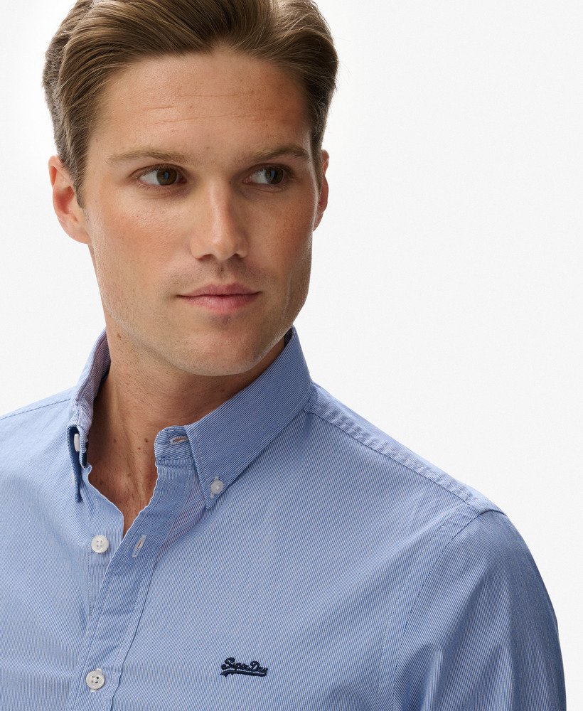 Man wearing a light blue shirt with a visible brand logo on a plain background