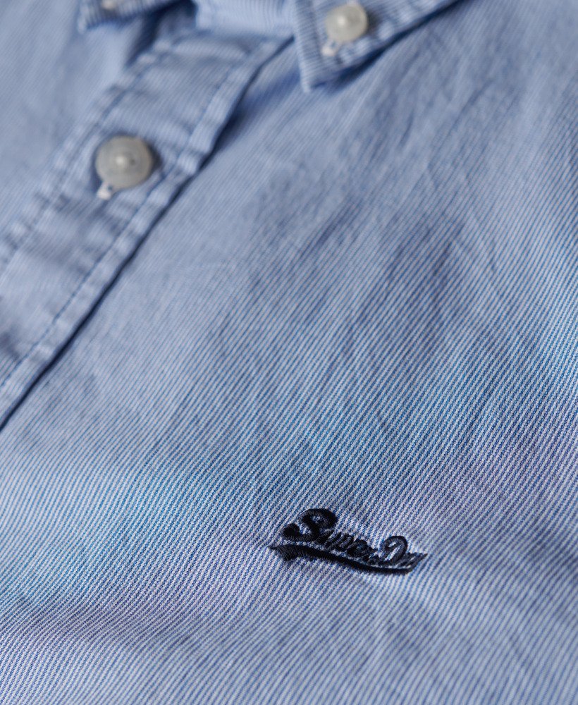 Close-up of a blue denim shirt with a brand logo on the chest.