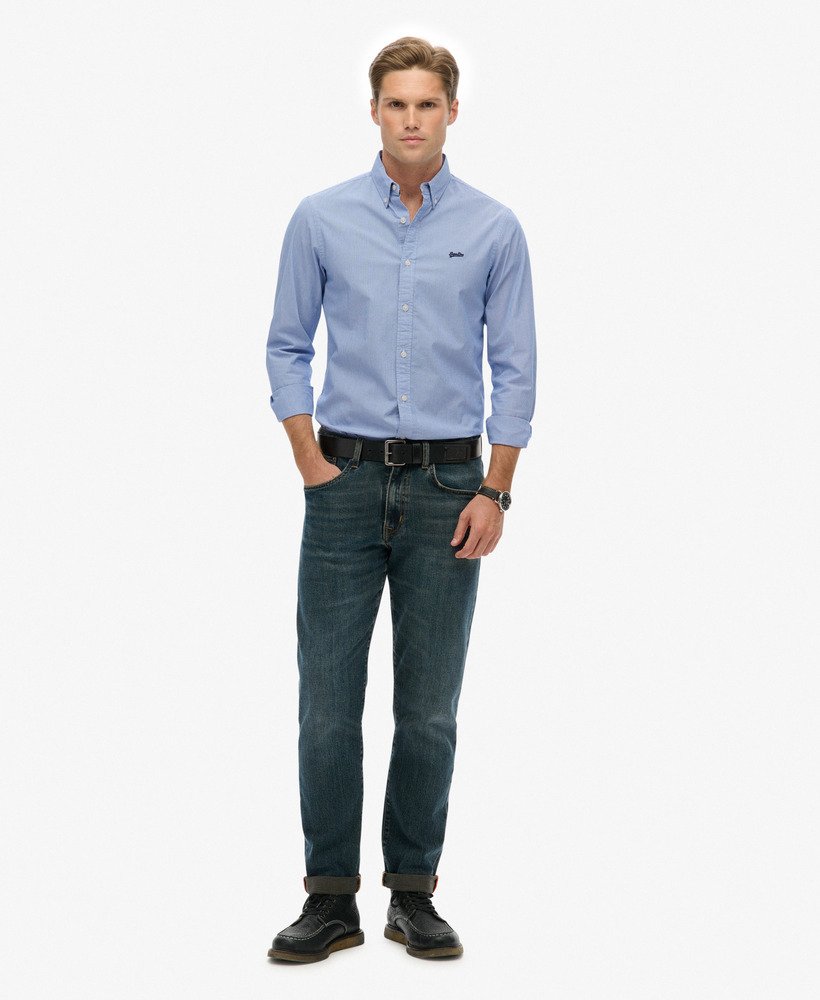 Man wearing a light blue button-up shirt and dark jeans on a white background