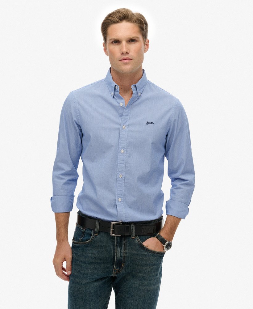 Man wearing a light blue button-up shirt with a logo on a white background