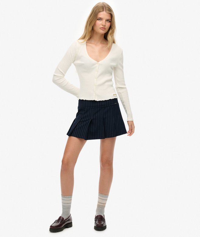 Woman wearing a white long-sleeve top and navy pleated skirt on a white background