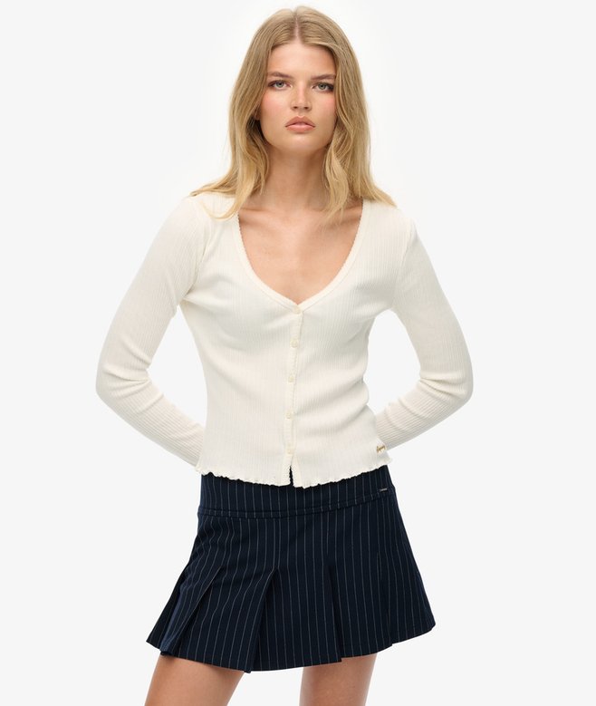 Woman wearing a white cardigan and navy pleated skirt on a white background