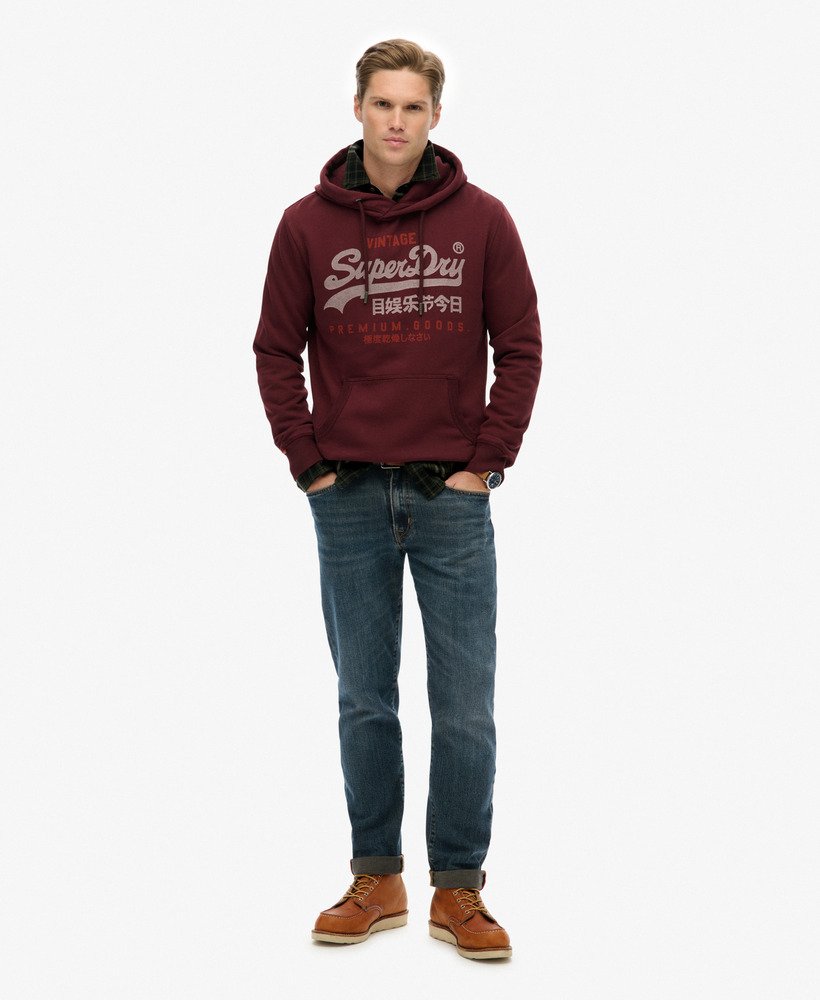 Man wearing a maroon hoodie with a logo, blue jeans, and brown boots on a white background