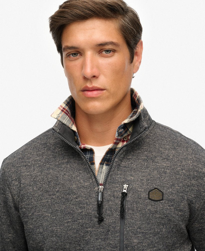 Man wearing a gray sweater with a plaid collar against a light gray background