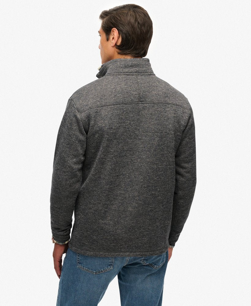 Man wearing a gray fleece jacket and blue jeans on a white background