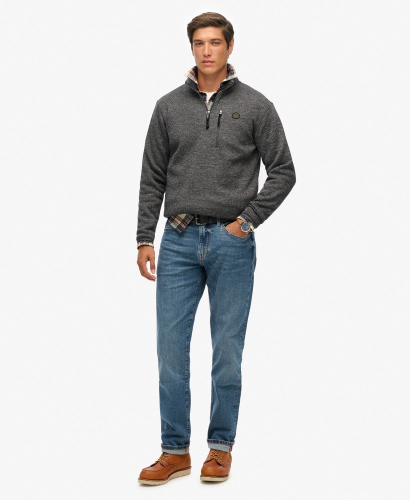 Man wearing a gray sweater, blue jeans, and brown boots on a white background