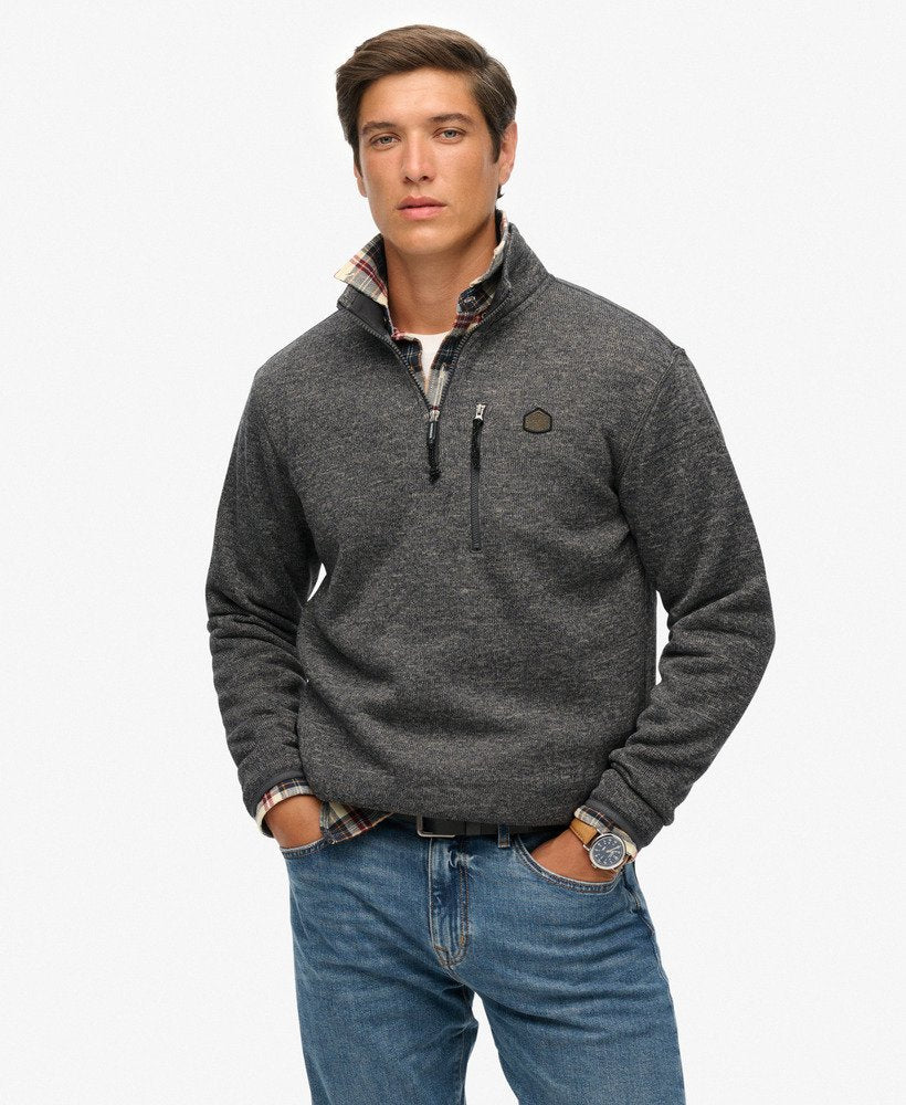 Man wearing a gray pullover with a plaid shirt underneath on a white background