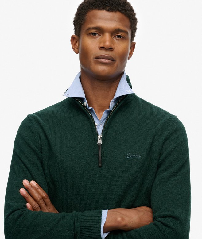 Man wearing a green sweater with a blue shirt underneath on a plain background