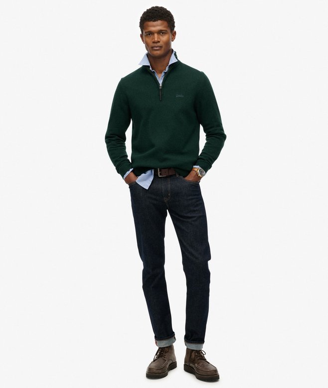 Man wearing a green sweater, white shirt, dark jeans, and brown shoes on a white background