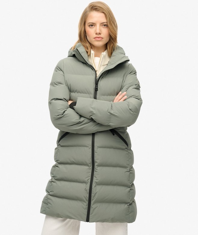 Woman wearing a long green puffer coat on a white background