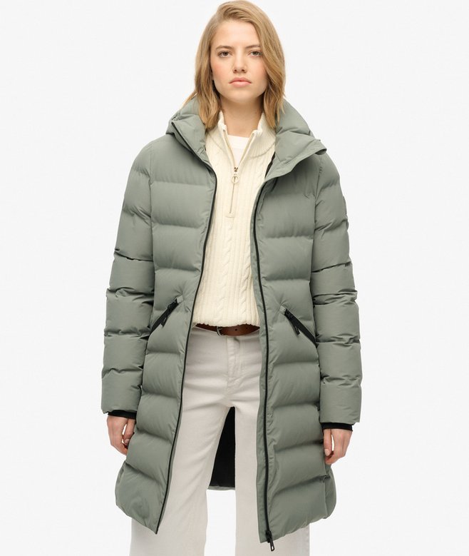 Woman wearing a long green puffer coat on a white background