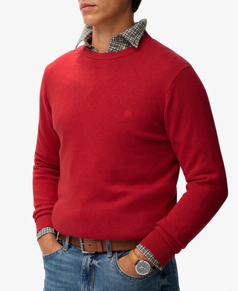 Person wearing a red sweater with plaid shirt collar and jeans on a white background