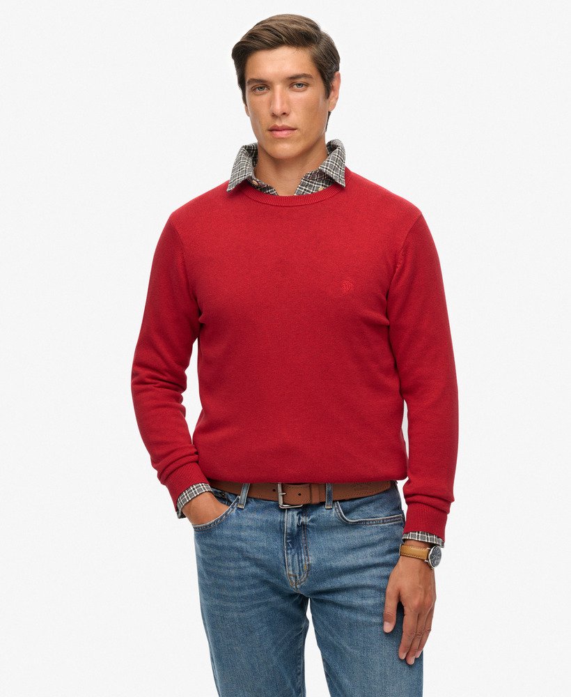 Man wearing a red sweater with a checkered collar, blue jeans, and a brown belt on a white background.