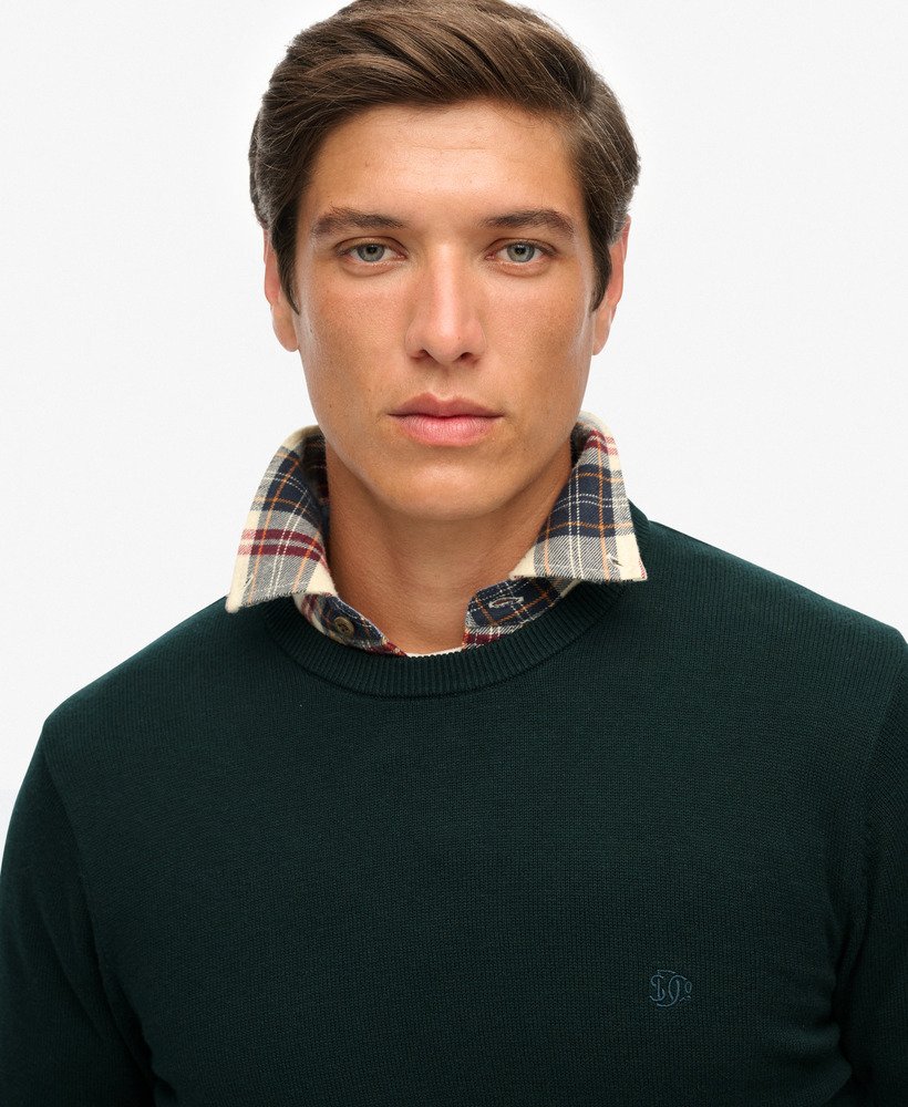 Man wearing a dark green sweater with a plaid shirt underneath on a white background