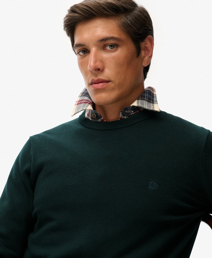 Man wearing a dark green sweater with a plaid shirt underneath on a white background