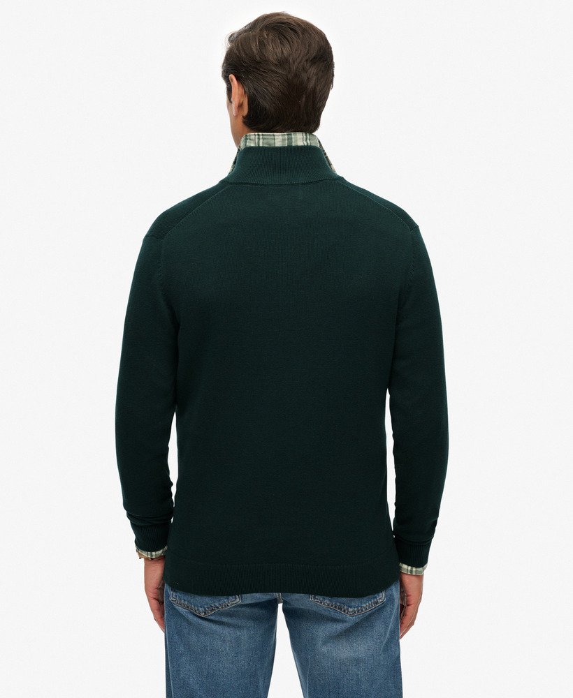 Man wearing a dark green quarter-zip sweater and blue jeans on a white background
