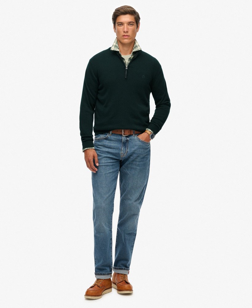 Man wearing a dark green sweater, blue jeans, and brown shoes on a white background