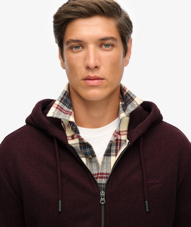 Man wearing a maroon hoodie with a plaid shirt underneath on a plain background