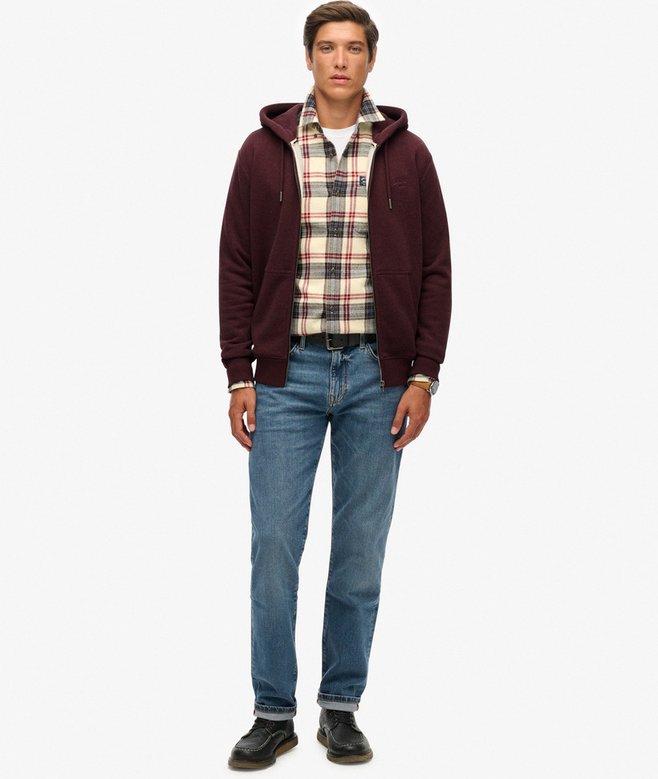 Man wearing a maroon hoodie, plaid shirt, and blue jeans on a white background