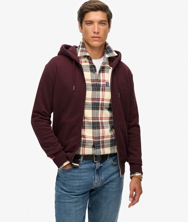 Man wearing a maroon hoodie over a plaid shirt with blue jeans on a white background