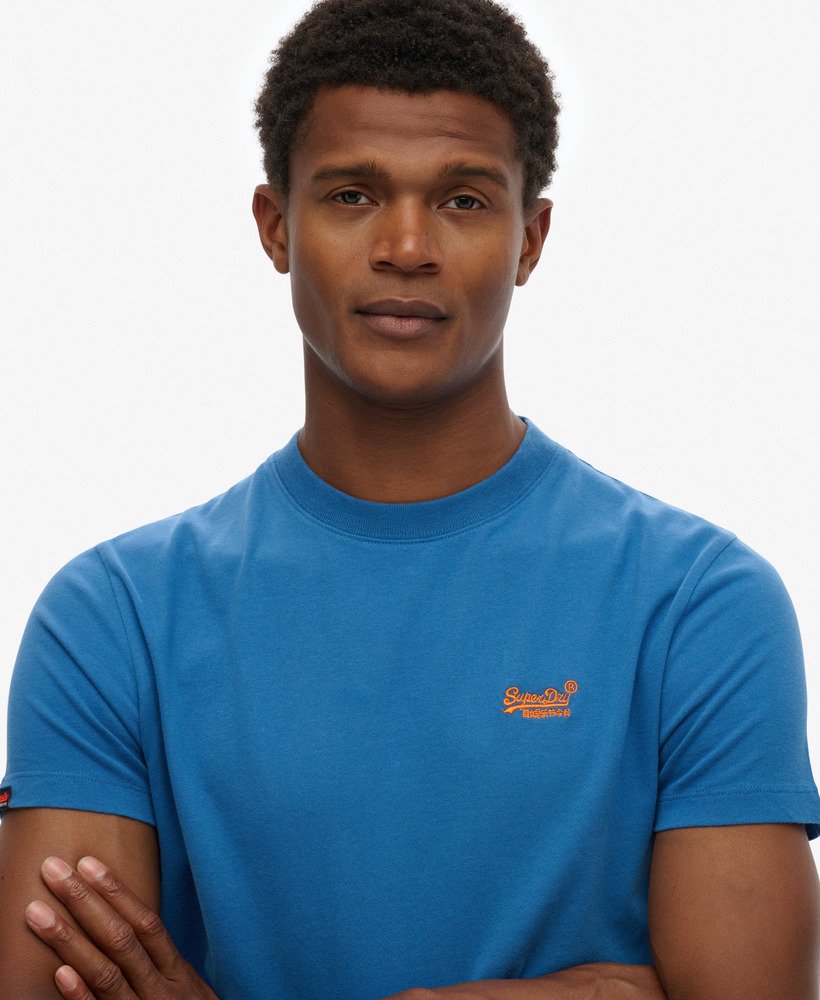 Man wearing a blue t-shirt with a logo on a plain background